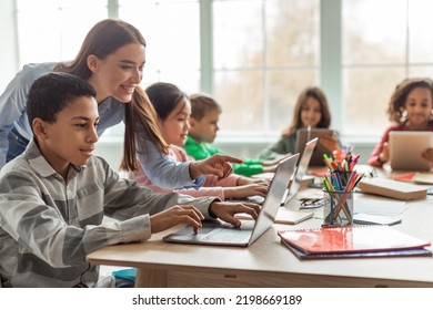 Teacher Teaching Diverse School Kids Using Laptop In Classroom. African American Schoolboy And Diverse Classmates Browsing Internet On Computer Learning Online Indoor. E-Learning Concept - Shutterstock ID 2198669189