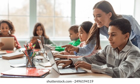 Teacher Teaching Diverse School Kids Using Laptop In Classroom. African American Schoolboy And Diverse Classmates Browsing Internet On Computer Learning Online Indoor. E-Learning Concept - Powered by Shutterstock