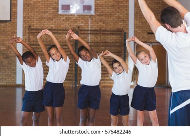 Teacher Teaching Exercise To School Kids In Basketball Court At School Gym