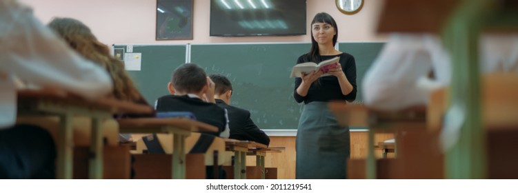 The teacher is teaching a lesson at school. Young woman teacher at a lesson in the classroom at the blackboard explains the lesson to children - Powered by Shutterstock