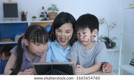 The teacher is testing the children with a tablet in the classroom, With a bright face.