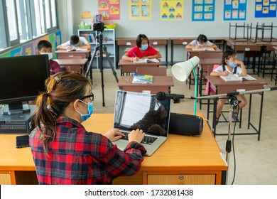 Teacher wearing protective mask to Protect Against Covid-19,Group of school kids with teacher sitting in classroom online and raising hands,Elementary school,Learning and people concept. - Powered by Shutterstock