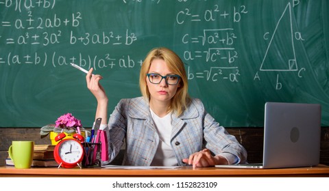 Teacher Woman Sit Table Classroom Chalkboard Background. Create And Distribute Educational Content. Present Lesson In Comprehensive Manner To Facilitate Learning. Promoting Interactive Learning.