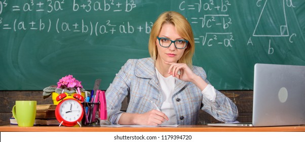 Teacher Woman Sit Table Classroom Chalkboard Background. Present Lesson In Comprehensive Manner To Facilitate Learning. Create And Distribute Educational Content. Promoting Interactive Learning.