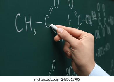 Teacher writing chemical formulas with chalk on green chalkboard, closeup - Powered by Shutterstock