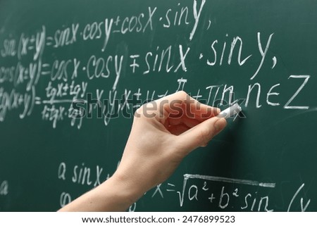 Teacher writing down math equation on green board, closeup