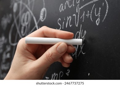 Teacher writing math formulas with chalk on blackboard, closeup