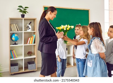 Teacher's Day. Schoolchildren congratulating their female teacher and giving her flowers in school classroom. Happy woman accepts bouquet of tulips from her little students. Concept of school holidays - Powered by Shutterstock