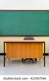 Teacher's Desk Behind A Wooden Writing Board.