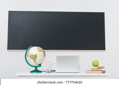 Teachers Desk With Laptop In Classroom In Front Of Chalkboard