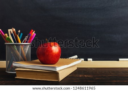 Teacher's desk with writing materials, a book and an apple, a blank for text or a background for a school theme. Copy space.