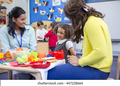 Teachers playing with plastic kitchen toys with their nursery students in the classroom.