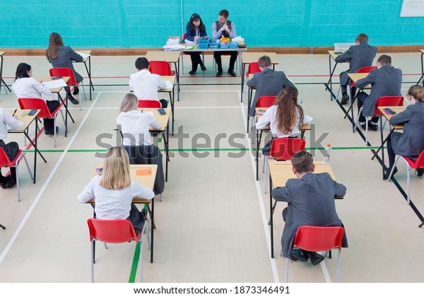 Teachers supervising middle school\
students taking examination at desks in school gymnastics\
hall