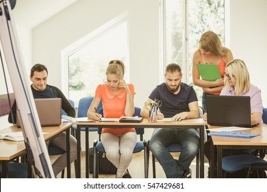 Teaching Concept. Female Young Teacher Or Tutor With Adult Students In Classroom With Papers, Laptop Computer. Studies Course