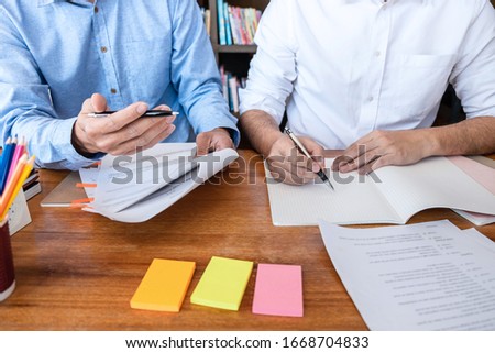 Teaching helping and study course, Team of young teacher or tutor helps students to learning in classroom for homework a test or exam at desk with papers.