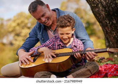 Teaching him a tune. Shot of a father teaching his son how to play guitar while sitting outside. - Powered by Shutterstock