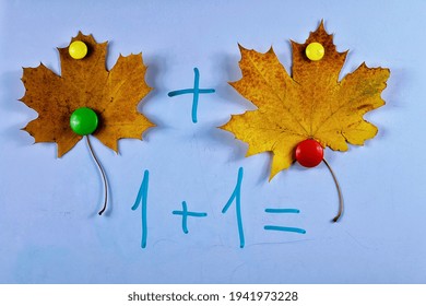 Teaching kids basic of math addition with the aid of magnets, yellow leaves of maple on the  blue board, example of educational math children game