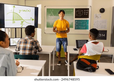 Teaching math, teacher using tablet in classroom with students at high school. Education, technology, learning, academic, instructor, children