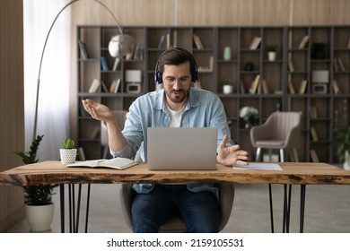 Teaching On Distance. Confident Male Teacher In Headset And Glasses Sit At Desk Give Remote Video Class In Conference App Using Laptop Webcam. Young Man Tutor Coach Talk Before Pc Hold Online Training