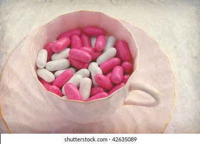 Teacup full of pink and white candy pills on a textured background.