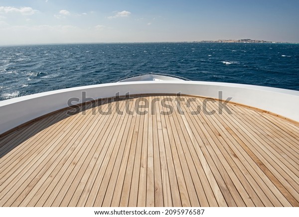 Teak bow deck of a large luxury\
motor yacht out at sea with a tropical ocean view\
background