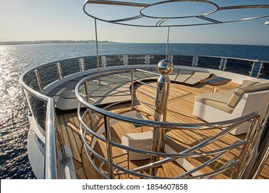 Teak stern deck of a large luxury motor yacht with sunbeds chairs sofa and tropical sea view background