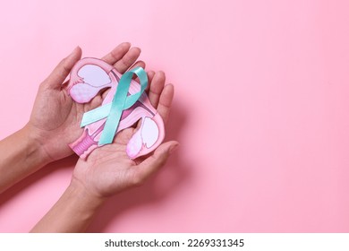 Teal awareness ribbon with cervix shape on palms hand over pink background with copy space. Ovarian Cancer month, cervical cancer day.  - Shutterstock ID 2269331345