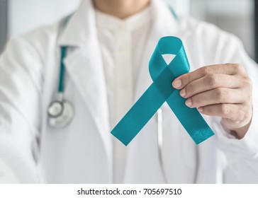 Teal awareness ribbon in doctor's hand, symbolic bow color for supporting patient with Ovarian Cancer, Polycystic Ovary Syndrome (PCOS) and Post Traumatic Stress Disorder (PTSD) Illness awareness 