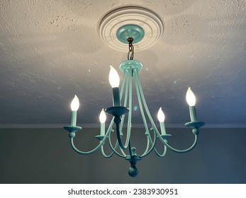 A teal colored hanging light fixture with 5 bulbs, attached to the white ceiling. The color of the chandelier makes it look like an antique. - Powered by Shutterstock