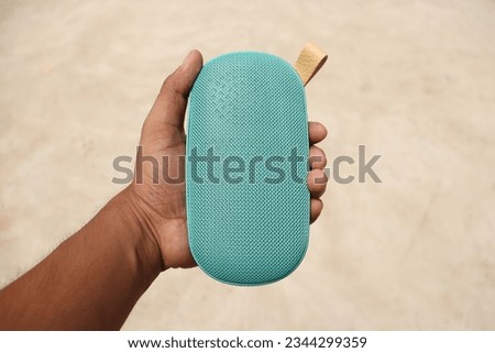 A Teal colour wireless handy pocket speaker held in a Hand vertically in an isolated background 