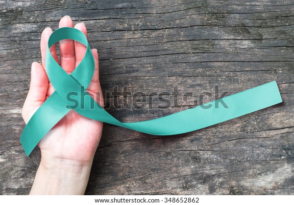 Teal ribbon awareness on woman\'s hand for Ovarian\
Cancer, Polycystic Ovary Syndrome (PCOS) disease, Post Traumatic\
Stress Disorder (PTSD), Tourette\'s Syndrome, Obsessive Compulsive\
Disorder (OCD) 
