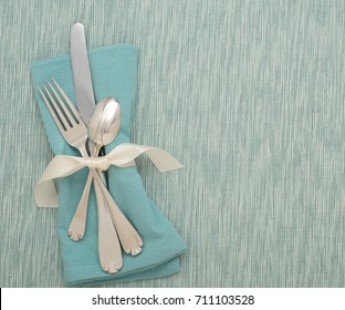 Teal Table Place Setting With Silverware, Turquoise Cloth Napkin On A Cyan, Textured Tablecloth Or Mat With Room Or Space For Copy, Test Or Words. A Horizontal With Flay Lay, Overhead Above View.