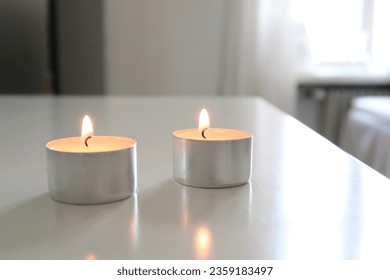 Tealight on a white table, neutral tones, white home, minimalistic studio apartment, no people, candlelight fire, calm atmosphere, flicker light of a small candle, winter aesthetics, neutral tones - Powered by Shutterstock