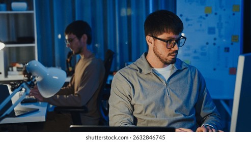 Team adult male freelance developer work late typing write prompt AI bot app program nomad terminal code at office night. Artificial intelligence dashboard, robotics, user interface, machine learning.