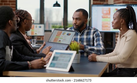 Team Of African American Employees Analyzing Financial Charts On Laptop Screen, Doing Teamwork To Plan Business Growth. People Working On Project Collaboration, Using Computer And Digital Tablet.