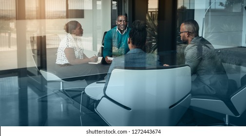 Team of african bussines people talking during an work meeting shot through a glass window, looking into the boardroom