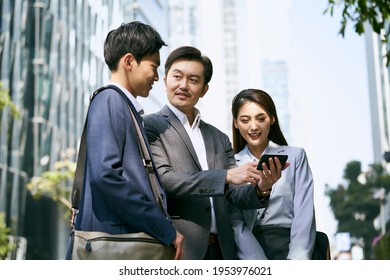 a team of asian business people standing in street having a discussion using cellphone in city downtown