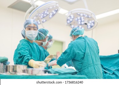 Team of Asian doctor doing surgery inside modern operating room. Surgeon in green surgical gown suit under surgical lamp. Selective focus at nurse 's hand that prepare implant for surgeon. - Powered by Shutterstock