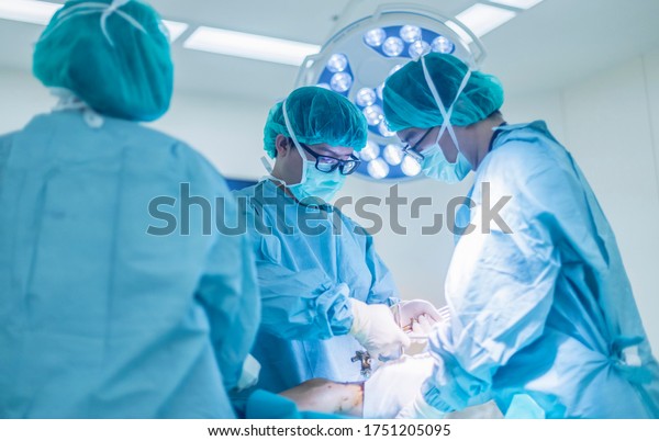 Team of Asian doctor doing surgery inside modern\
operating room. Surgeon in green surgical gown suit under surgical\
lamp. Bone fracture fixation was done in car accident patient.\
Uprisen angle.