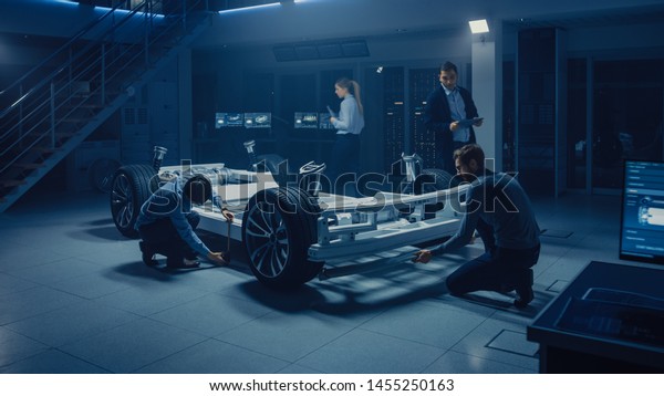 Team of Automotive Engineers Working on Electric
Car Platform Chassis, Taking Measures, working with 3D CAD
Software, Analysing Efficiency. Vehicle Frame with Wheels, Engine
and Battery.