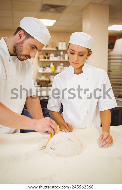 Team of\
bakers kneading dough in a commercial\
kitchen