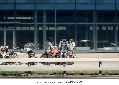 A team of bikers in leather jackets and helmets resting near highway behind the road iron bumper.