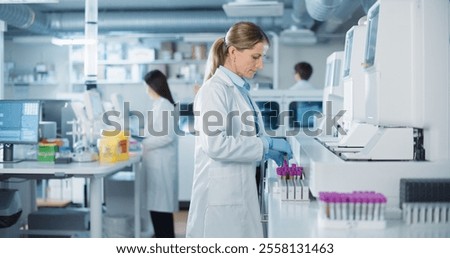 Team of Biomedical Engineers Work in a Lab. Senior Researcher Adding Samples to Test Machine, Asian Female Adjusting Settings on a Digital Microscope while Male Colleague Carrying Medical Glassware