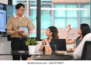 Team brainstorming user interface project while colleague raises hand to ask a question