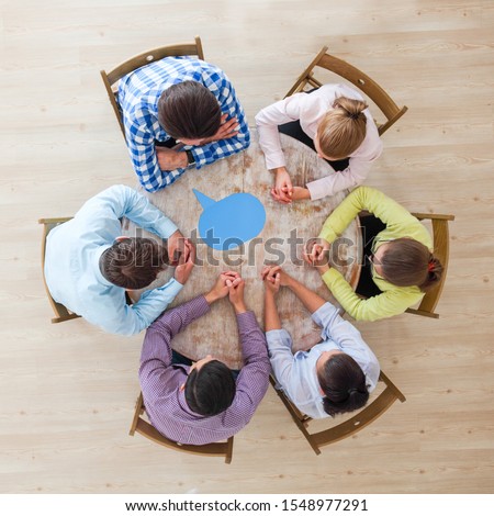 Team of business people in casual clothes sitting around the table with paper dialog boxes, discussing opinion concept