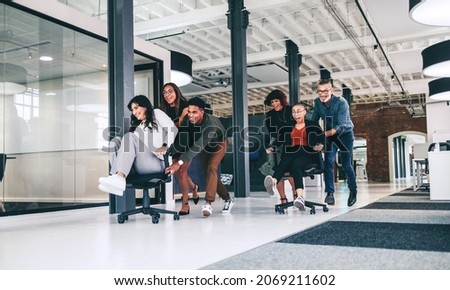 Team of businesspeople having fun together in an office. Cheerful group of colleagues pushing each other on chairs in a modern workplace. Businesspeople having fun and celebrating their success.