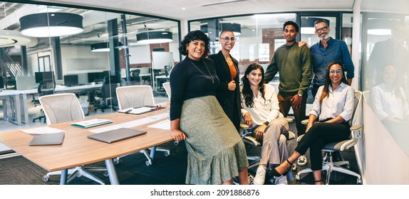 Team of businesspeople smiling at the camera in a boardroom. Cheerful businesspeople grouped together in a modern workplace. Diverse team of businesspeople looking cheerful. - Shutterstock ID 2091886876