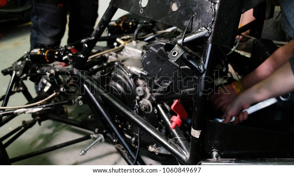 The team of car mechanics removes the\
internal combustion engine from the race\
car.