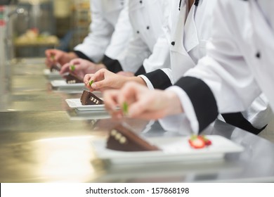 Team of chefs garnishing dessert plates in a busy kitchen - Powered by Shutterstock