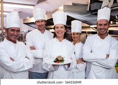 Team of chefs in the kitchen with one presenting a dish - Powered by Shutterstock